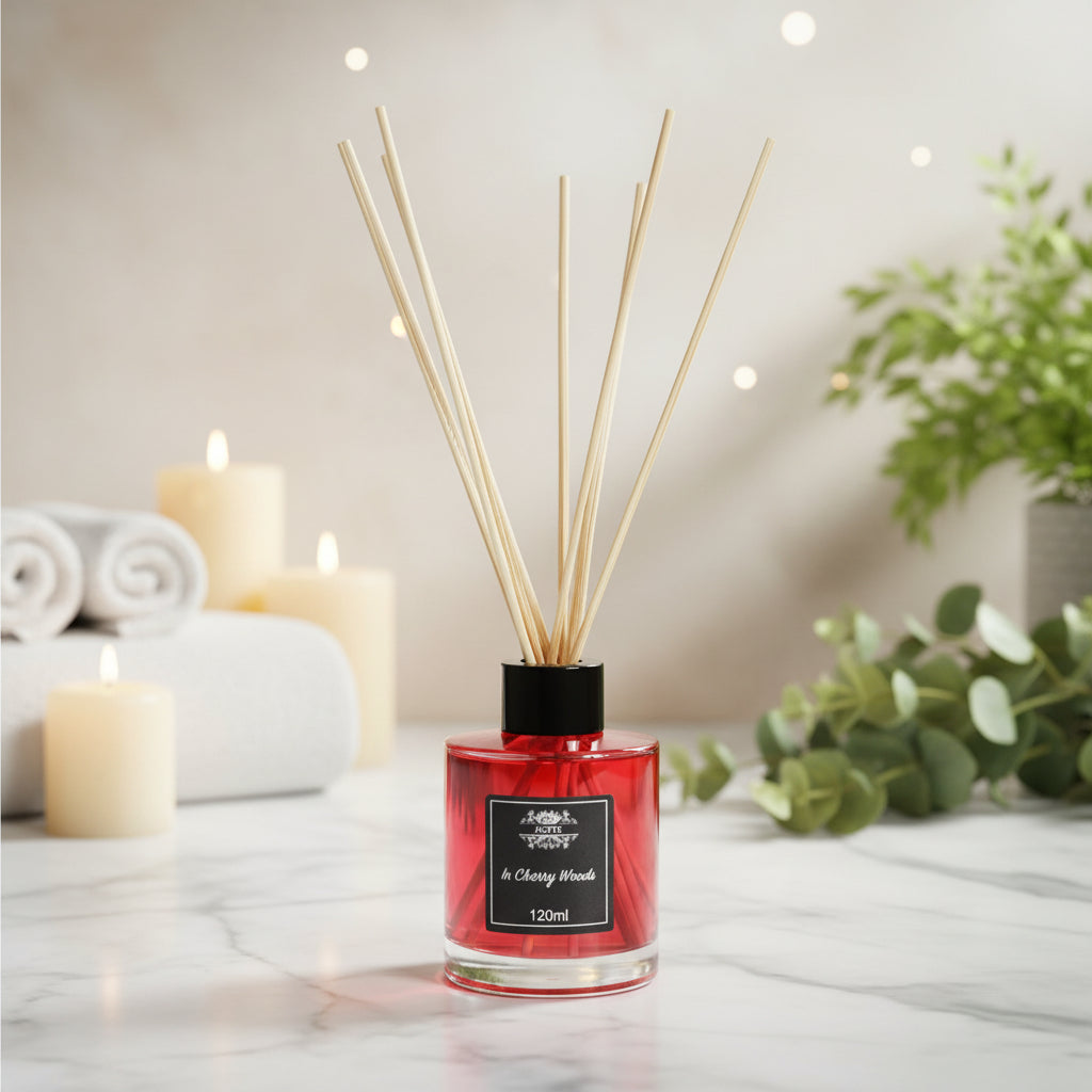 Red diffuser with wooden sticks on a marble surface with candles and plants in the background