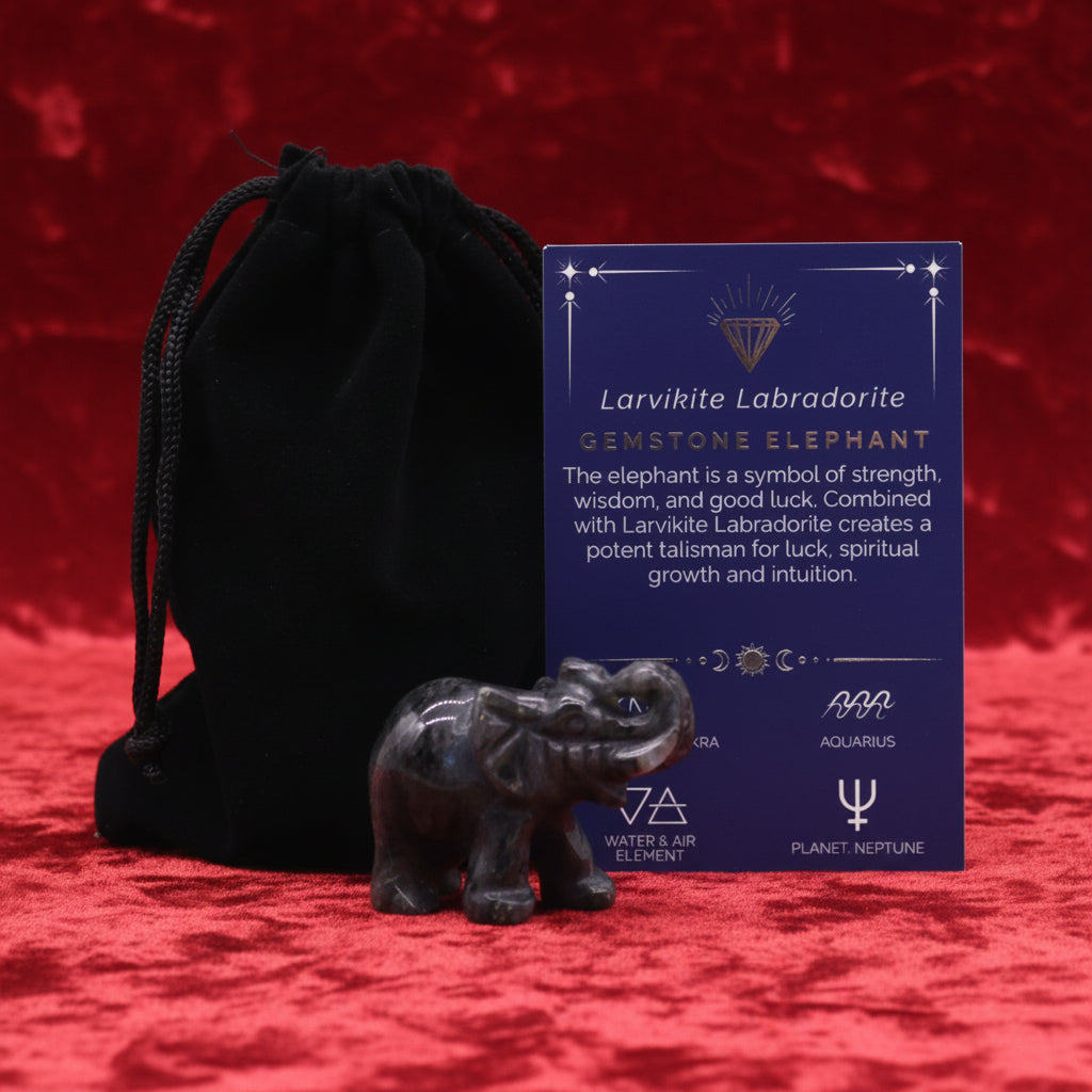 A hand-carved gemstone elephant next to a black velvet pouch and a card detailing the properties of the gemstone.