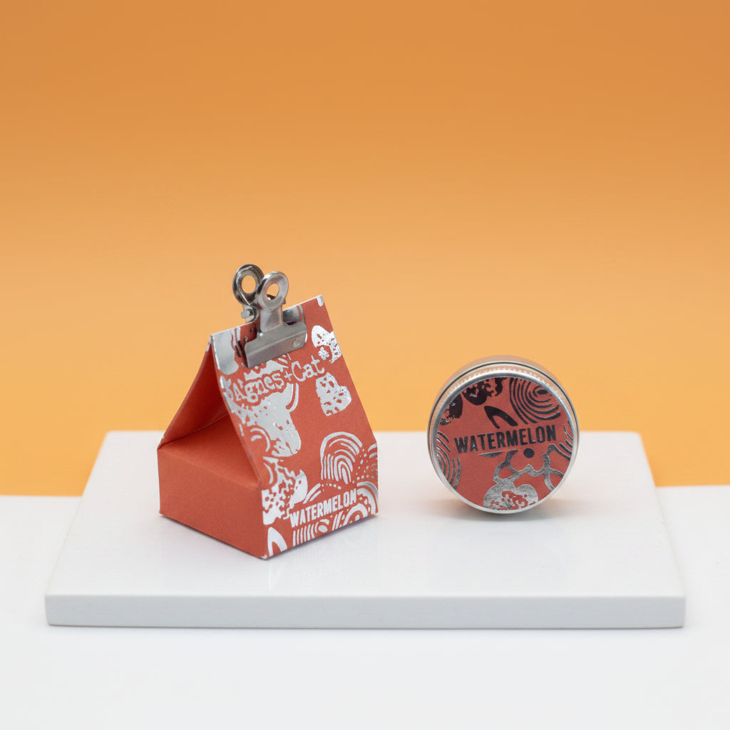 A triangular orange packaging of Agnes and Cat lip balm with a clip on top and 'Watermelon' text on the front.