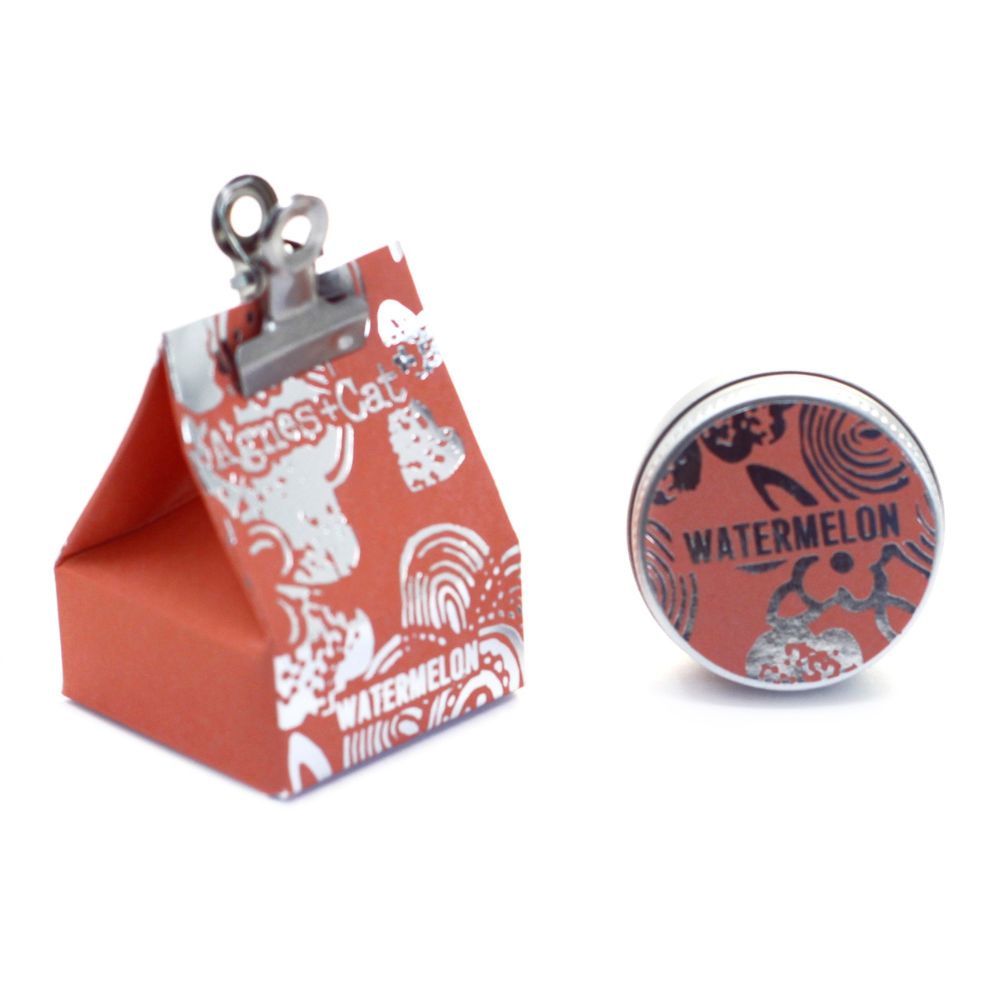 A triangular orange packaging of Agnes and Cat lip balm with a clip on top and 'Watermelon' text on the front.