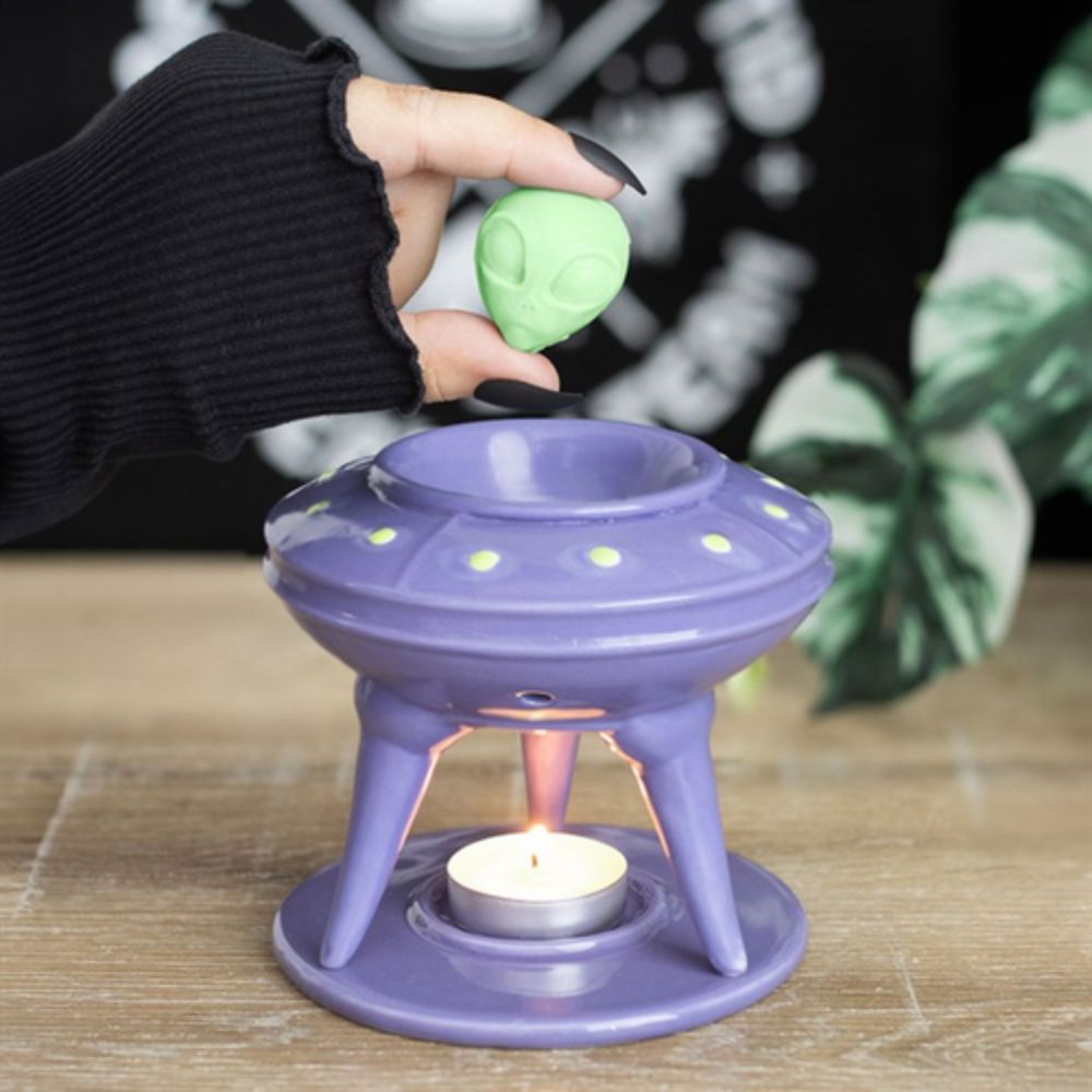 Purple oil burner with a lit candle inside, held by a gloved hand over a blurred background.