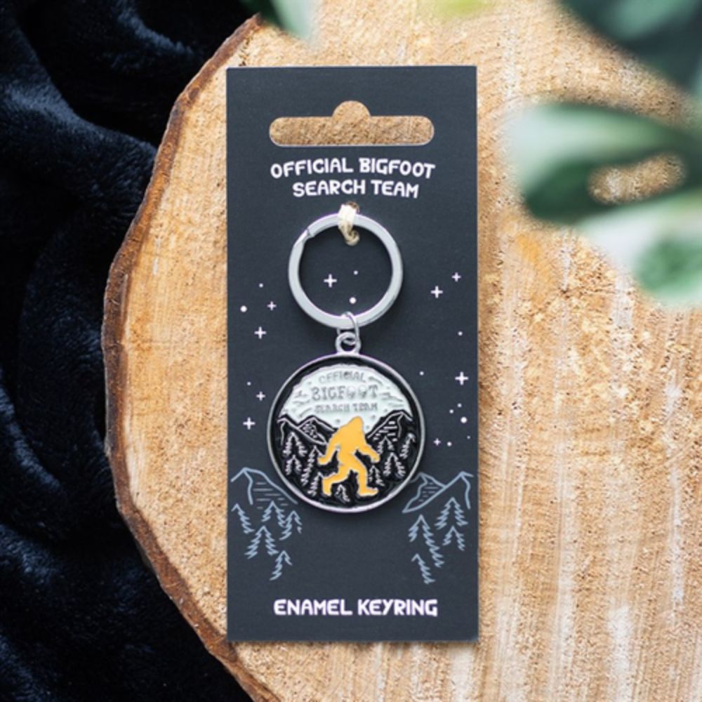 Keyring with Bigfoot design on a branded card, placed on a wooden surface.
