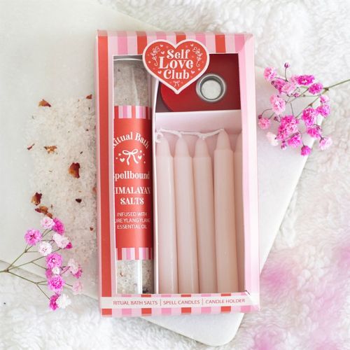 Packaged product from Self Love Club with bath salts and candles on a textured surface with flowers.