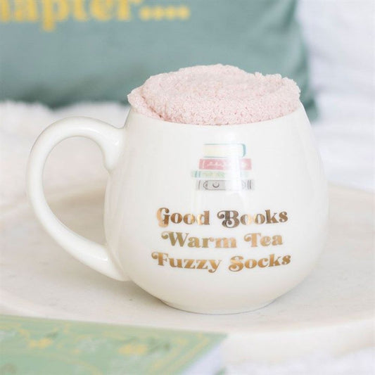White mug with text 'Good Books Warm Tea Fuzzy Socks' on a soft surface.