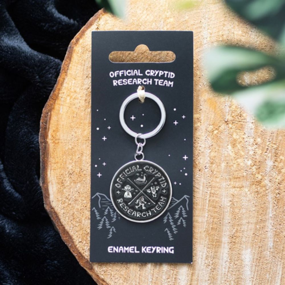 Enamel keyring on a 'Official Cryptid Research Team' card on a wooden surface
