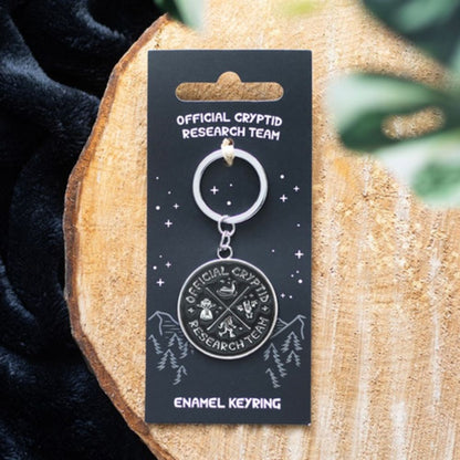 Enamel keyring on a 'Official Cryptid Research Team' card on a wooden surface