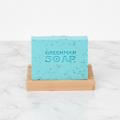 Greenman Soap bar on a wooden soap dish with a white background