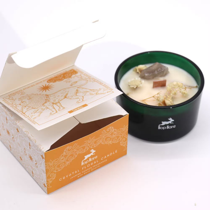 Candle in a black container with floral elements next to its packaging on a white background