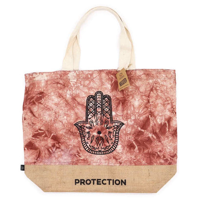 Tote bag with Hamsa hand design and 'PROTECTION' text on a pink and beige patterned background.