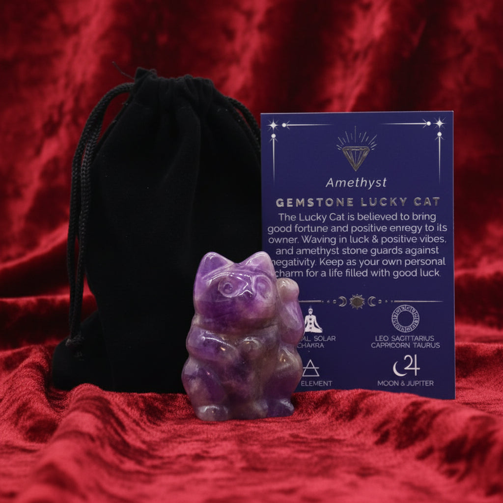 A hand-carved purple gemstone in the shape of a lucky cat, accompanied by a black velvet pouch and a card with details about the gemstone.