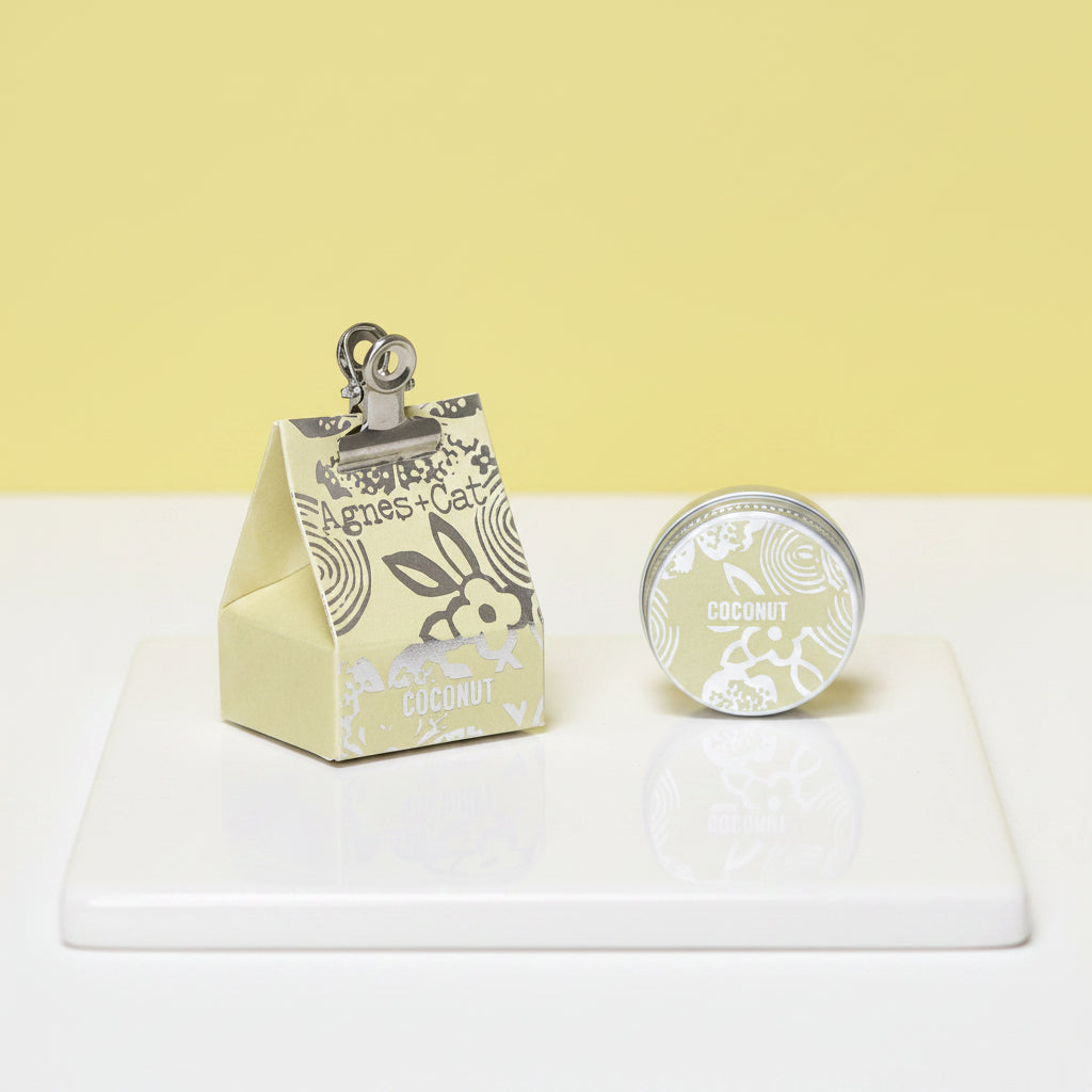 A triangular lemon packaging of Agnes and Cat lip balm with a clip on top and 'coconut' text on the front.