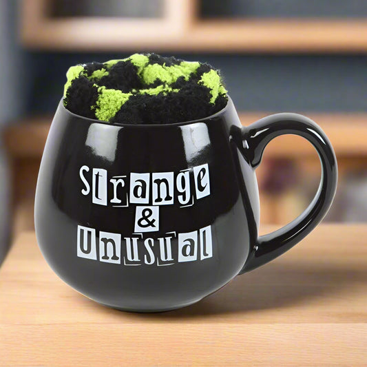 Black mug with text 'Strange & Unusual' and a green and black patterned item inside on a white background