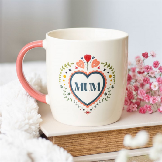 Mug with 'MUM' design on a surface with flowers and book