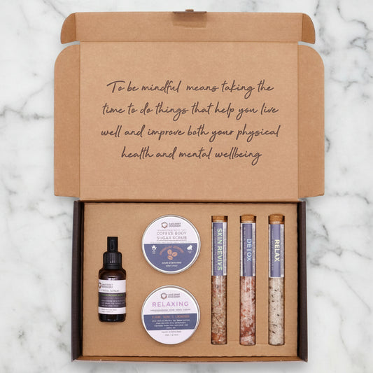 A self-care gift set box containing various bath products including a bottle, possibly of essential oil or perfume, and tubes with scrub and lotion.